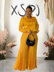 Elegant women's autumn outfit with a long sleeve button-up top and pleated pants in luxurious gold.